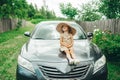 Cute little girl in hat sitting on car hood, looking to sides Royalty Free Stock Photo