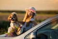 Cute little girl in a hat sitting on the hood of the car next to a dog and a bouquet of flowers. Royalty Free Stock Photo