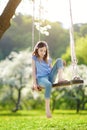 Cute little girl having fun on a swing in blossoming old apple tree garden outdoors on sunny spring day. Royalty Free Stock Photo