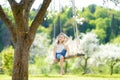 Cute little girl having fun on a swing in blossoming old apple tree garden outdoors on sunny spring day Royalty Free Stock Photo