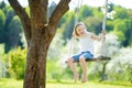 Cute little girl having fun on a swing in blossoming old apple tree garden outdoors on sunny spring day. Royalty Free Stock Photo