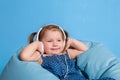 Cute little girl in headphones listening to music using a tablet and smiling while sitting on blue big bag Royalty Free Stock Photo