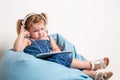 Cute little girl in headphones listening to music using a tablet and smiling while sitting on blue big bag Royalty Free Stock Photo