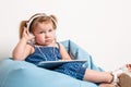 Cute little girl in headphones listening to music using a tablet and smiling while sitting on blue big bag Royalty Free Stock Photo