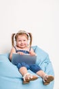 Cute little girl in headphones listening to music using a tablet and smiling while sitting on blue big bag Royalty Free Stock Photo