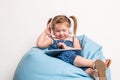 Cute little girl in headphones listening to music using a tablet and smiling while sitting on blue big bag Royalty Free Stock Photo