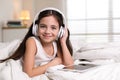 Cute girl with headphones and tablet listening to audiobook in bed at home