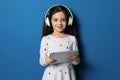 Cute little girl with headphones and tablet listening to audiobook on background