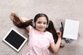 Cute little girl with headphones and tablet listening to audiobook on floor, flat lay