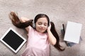 Cute little girl with headphones and tablet listening to audiobook on floor indoors