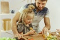 Cute little girl and her beautiful parents are cutting vegetables in kitchen at home Royalty Free Stock Photo