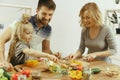 Cute little girl and her beautiful parents are cutting vegetables in kitchen at home Royalty Free Stock Photo