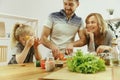 Cute little girl and her beautiful parents are cutting vegetables in kitchen at home Royalty Free Stock Photo