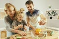 Cute little girl and her beautiful parents are cutting vegetables in kitchen at home Royalty Free Stock Photo