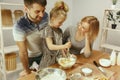 Cute little girl and her beautiful parents preparing the dough for the cake in kitchen at home Royalty Free Stock Photo