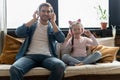 Cute little girl and her handsome father in headphones are listening to music, smiling, sitting on couch at home. Royalty Free Stock Photo