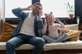 Cute little girl and her handsome father in headphones are listening to music, smiling, sitting on couch at home. Royalty Free Stock Photo