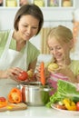 Cute little girl with her mother cooking together at kitchen table Royalty Free Stock Photo