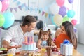 Cute little girl and her parents celebrating birthday at table with cake