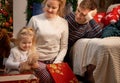 Cute little girl with her young parents celebrating Christmas at home by the fireplace
