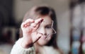 Cute little girl holding big christmas star and looking through it. Royalty Free Stock Photo