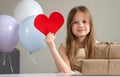 Cute little girl holding big red heart surrounded by zero waste gifts and air balloons. Holiday greetings Valentines Day