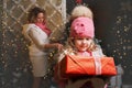 Cute little girl holding a Christmas present in her hands. in the background mom is decorating the tree Royalty Free Stock Photo