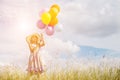 Cute little girl holding colorful balloons in the meadow against blue sky and clouds,spreading hands Royalty Free Stock Photo