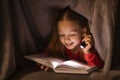 Cute Little Girl Holding Flashlight And Reading Book Under Blanket At Home Royalty Free Stock Photo