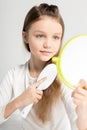 Cute little girl holding hand mirror and combing hair