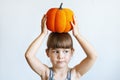 A cute little girl is holding a pumpkin on her head. A beautiful baby with a pumpkin on her head is a symbol of the Halloween Royalty Free Stock Photo