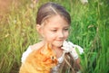 Cute little girl is holding a red cat sitting in the grass.