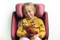 Cute little girl holding stuffed Rudolph Red-Nosed Reindeer toy while sitting in a safety car seat.