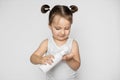 Cute little girl holding white plastic bottle in her hands, and pouring oil or cream milk, looking at the bottle. Baby Royalty Free Stock Photo