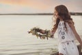Cute little girl holding wreath made of beautiful flowers near river in evening Royalty Free Stock Photo