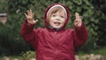 Cute little girl in a hooded jacket is happy and makes faces in front of camera Royalty Free Stock Photo