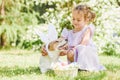 Cute little girl hugging her pet dog wearing Easter bunny ears costume. Basket with decorated eggs and flowers Royalty Free Stock Photo