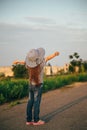 Cute little girl in jeans, striped shirt and sun hat standing at the road, raising hands with an exciting feeling of Royalty Free Stock Photo