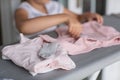 Cute little girl is leaning on ironing clothes on board at home. Daughter helping to mother ironing clothes for baby Royalty Free Stock Photo