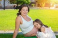 Cute little girl listening to her mothers pregnant belly in summer nature