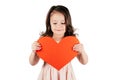 Cute little girl with long curly hair hold in hands big red paper heart lowering eyes forcing smile on white background. Royalty Free Stock Photo