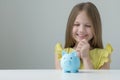 Cute little girl looking with hope and joy at piggy bank. Adorable child with money box. Copy space Royalty Free Stock Photo