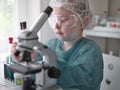 Cute little girl looking into microscope at his desk at home. Young scientist making experiments in his home laboratory Royalty Free Stock Photo