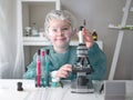 Cute little girl looking into microscope at his desk at home. Young scientist making experiments in his home laboratory Royalty Free Stock Photo