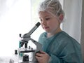 Cute little girl looking into microscope at his desk at home. Young scientist making experiments in his home laboratory Royalty Free Stock Photo