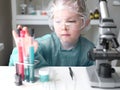 Cute little girl looking into microscope at his desk at home. Young scientist making experiments in his home laboratory Royalty Free Stock Photo