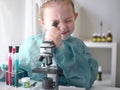 Cute little girl looking into microscope at his desk at home. Young scientist making experiments in his home laboratory Royalty Free Stock Photo