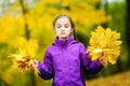 Cute little girl making funny faces on beautiful autumn day at city park. Funny child picking autumn leaves on sunny day. Royalty Free Stock Photo