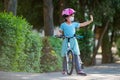 Cute little girl with mask on face ridding a bike and salute other kids from distance