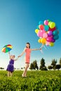 Cute little girl with mother colored balloons and rainbow umbrella holding in the park. Smiling child and mom on a field with fl Royalty Free Stock Photo